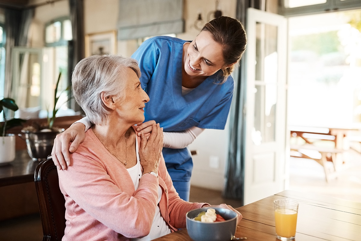 Woman with nurse with breakfast at her home and at the table in living room.