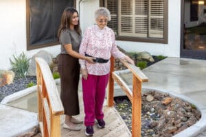 nurse assisting an elderly woman walking across a small bridge at auburn oaks care center